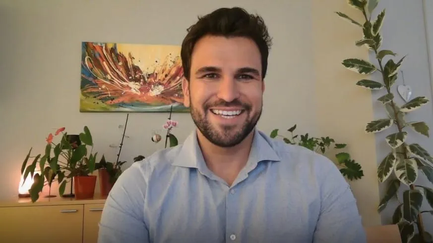 Lukas smiling in a room with houseplants and abstract wall art